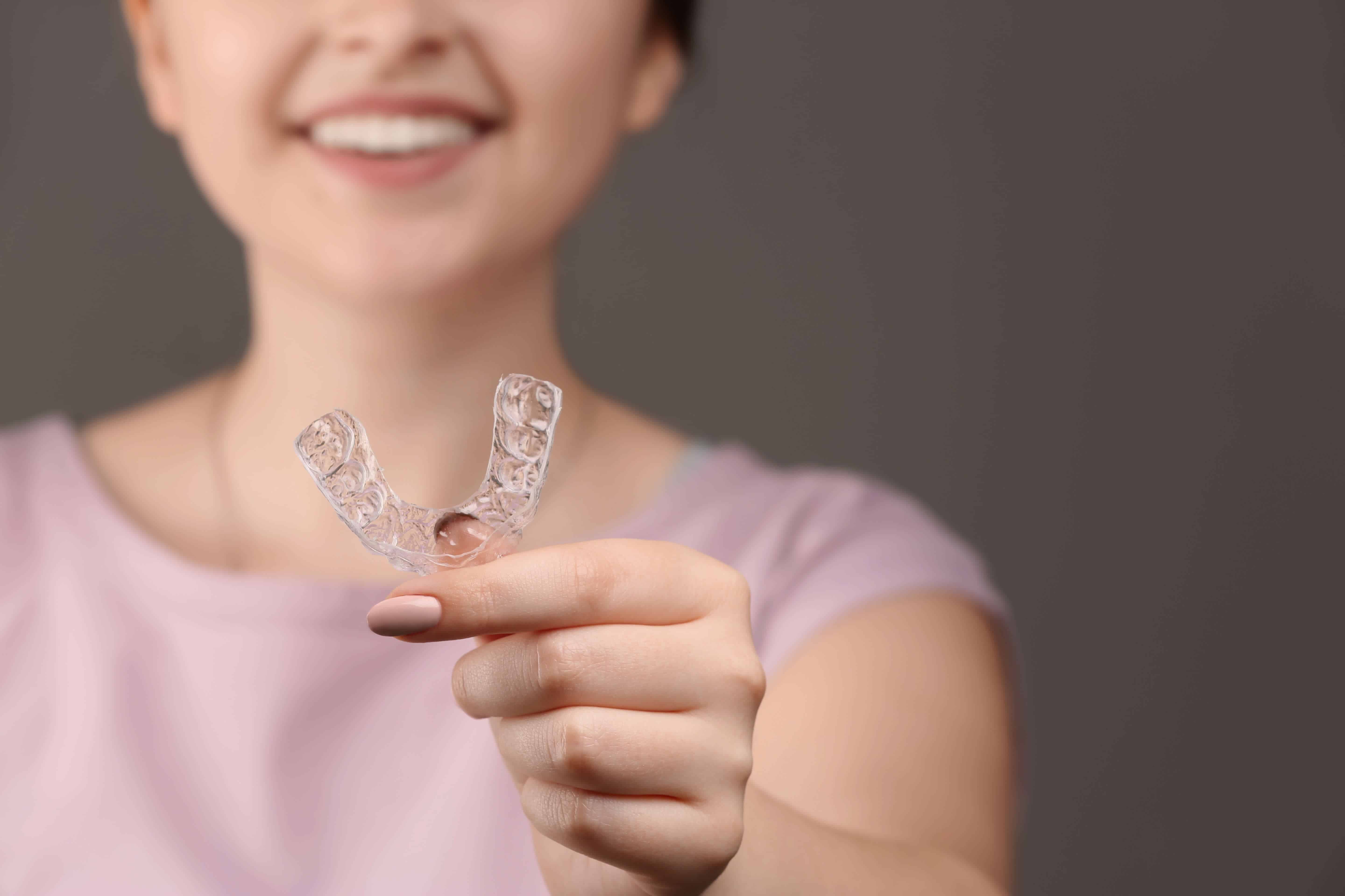 A smiling woman holding a clear dental aligner